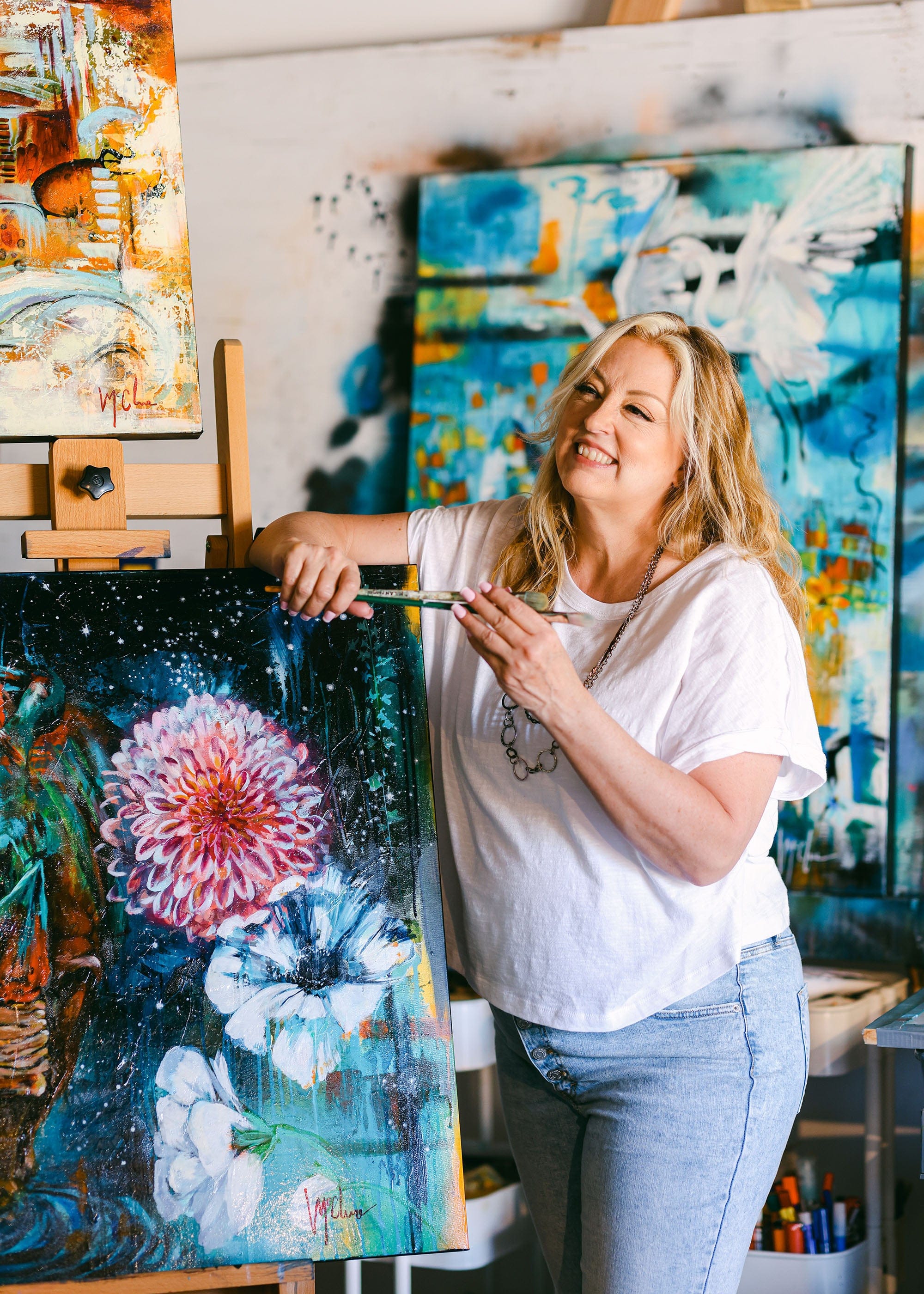Woman holding a paintbrush with a colorful painting of flowers in an art studio.