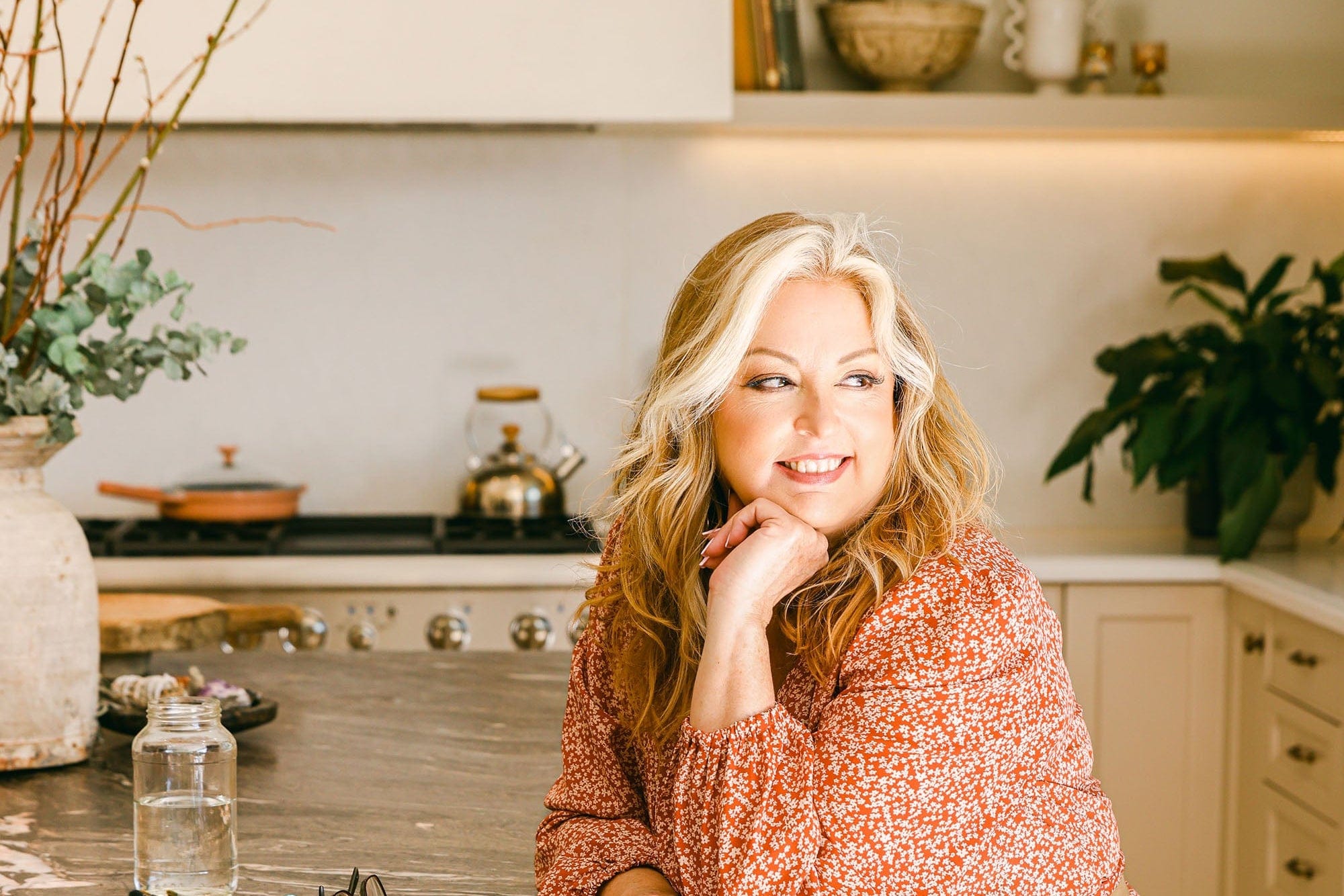 Woman in a kitchen wearing a floral dress, sitting on a counter.